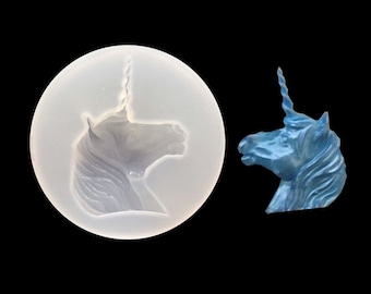 Op de afbeelding: Een witte siliconen mal voor het maken van een eenhoornhoofd. De mal wordt getoond naast een blauw eenhoornhoofd.