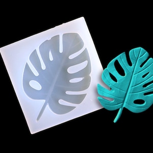 May include: A white silicone mold shaped like a monstera leaf, with a teal monstera leaf next to it.