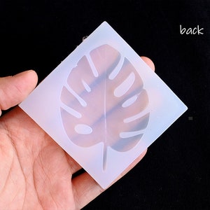 May include: A white silicone mold with a raised design of a monstera leaf. The mold is flexible and can be used to create resin crafts.