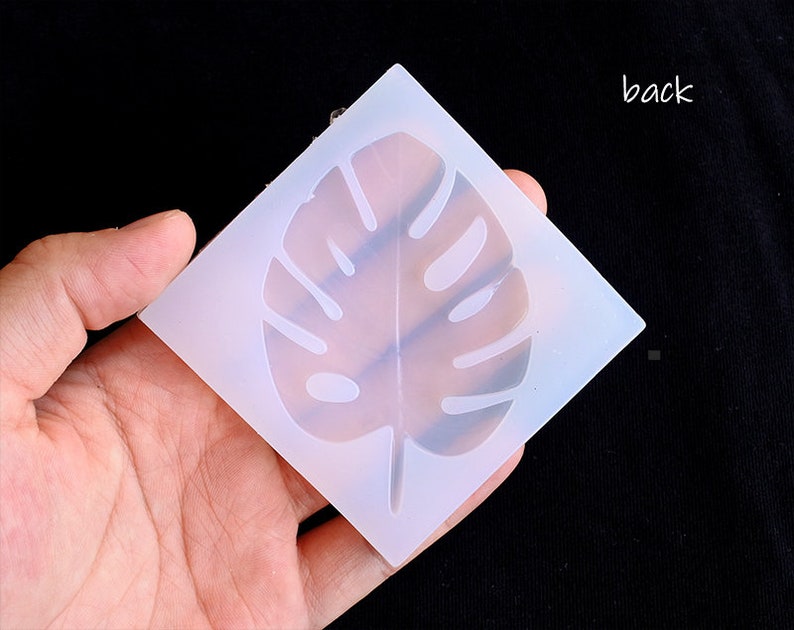 May include: A white silicone mold with a raised design of a monstera leaf. The mold is flexible and can be used to create resin crafts.
