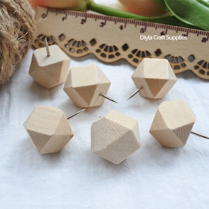 May include: Six wooden push pins in the shape of a geometric diamond with a silver pin. The push pins are on a white surface.
