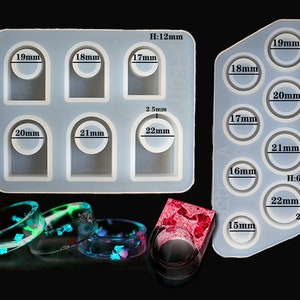 Peut inclure: Deux moules en silicone pour la fabrication d'anneaux en résine. Le moule de gauche comporte six cavités d'anneau de tailles 17 mm, 18 mm, 19 mm, 20 mm, 21 mm et 22 mm. Le moule de droite comporte sept cavités d'anneau de tailles 15 mm, 16 mm, 17 mm, 18 mm, 19 mm, 20 mm et 21 mm. Quatre anneaux en résine finis sont représentés au premier plan.