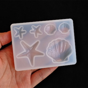 May include: A white silicone mould with five different shapes: two starfish, two seashells, and one large seashell. The mould is designed for making resin crafts.