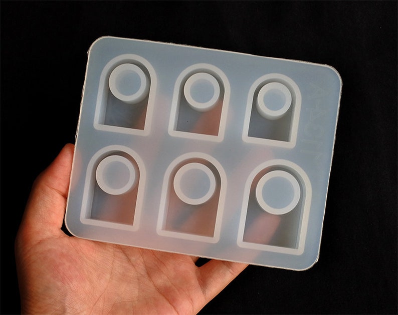 May include: A clear silicone mould with six rectangular cavities, each with a rounded top and a circular cutout in the centre. The mould is designed for making resin rings.