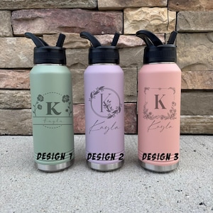 May include: Three personalized water bottles in pastel colors: green, lavender, and pink. Each bottle features a black flip-top lid and a silver base. The bottles are engraved with the letter "K" and the name "Kayla", surrounded by floral designs. The text "DESIGN 1", "DESIGN 2", and "DESIGN 3" are printed at the bottom.