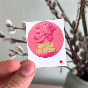 Könnte beinhalten: Ein runder Aufkleber mit einem rosa Porträt einer Person mit Krone und Schnurrbart und dem Text "GOD SAVE THE QUEERS" in Grün. Ein kleines Logo befindet sich in der unteren rechten Ecke.