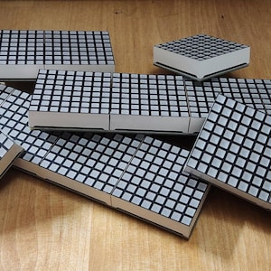 May include: A group of eight black and white LED dot matrix displays. The displays are arranged in a random pattern on a wooden surface.