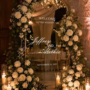 Puede incluir: Un espejo de boda arqueado con marco dorado y texto en blanco que dice WELCOME TO THE WEDDING OF Jeffrey AND Alethia SEPTEMBER 20, 2025. El espejo está decorado con rosas blancas y follaje, rodeado de portavelas cilíndricos de cristal.