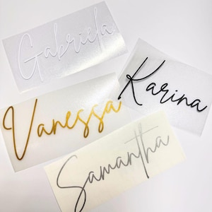 May include: Close-up of five name decals in various colours. The names are "Gabriela" in white, "Karina" in black, "Vanessa" in gold, and "Samantha" in silver. The decals are on a clear backing.