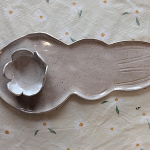 May include: A speckled, light grey ceramic serving platter with a flower-shaped dip bowl. The platter has a unique, elongated shape with a petal-like design at the end. The dip bowl is white and sits on a circular section of the platter.