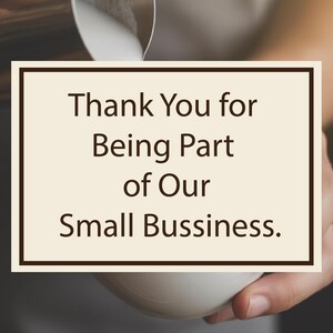 May include: A cream-coloured card with a dark brown border displays the text "Thank You for Being Part of Our Small Business." The card is held in a person's hand, with a white cup in the foreground.
