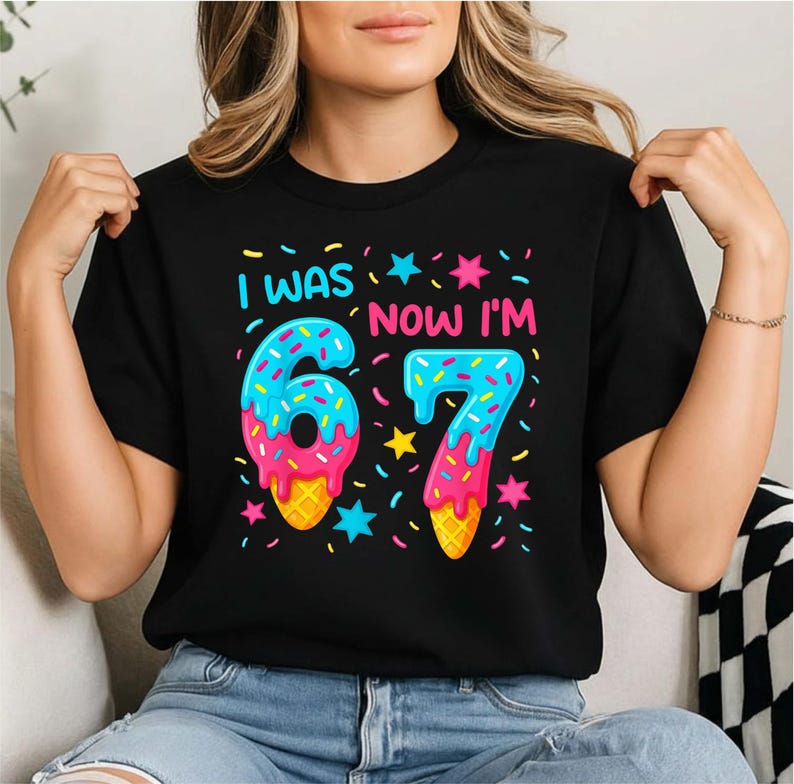 Peut inclure: T-shirt noir avec l'inscription "I WAS 6, NOW I'M 7" dans un design color&eacute; et ludique. Les chiffres sont stylis&eacute;s comme des c&ocirc;nes de cr&egrave;me glac&eacute;e avec des paillettes et des &eacute;toiles, parfait pour un anniversaire.