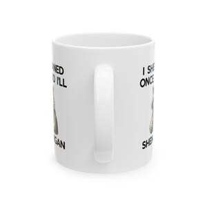 May include: White ceramic coffee mug with a curved handle. The mug features black text and a graphic of a dog. The text on the mug reads "I She Once Ned I'll Gan Shen".