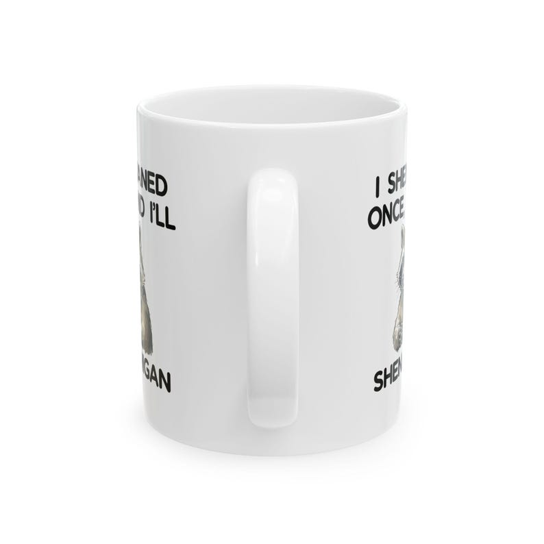 May include: White ceramic coffee mug with a curved handle. The mug features black text and a graphic of a dog. The text on the mug reads "I She Once Ned I'll Gan Shen".
