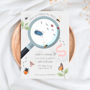 Könnte beinhalten: Eine hellgraue Einladungskarte mit einem Lupen-Design, die verschiedene Insekten zeigt. Der Text lautet "Have you heard the BUZZ..." und "HENRY IS TURNING 7!" mit Veranstaltungsdetails. Die Karte liegt auf einem Holztablett.