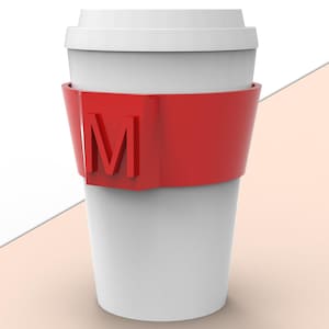 Può includere: Una tazza da viaggio bianca con una fascia rossa con la lettera "M". La tazza ha un coperchio bianco ed è progettata per bevande calde o fredde. Un'alternativa riutilizzabile alle tazze usa e getta.