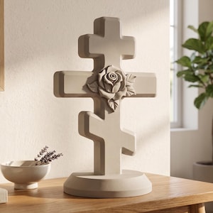 May include: A gray, three-barred Eastern Orthodox cross with a rose carving. The cross is made of a solid material and stands on a round base. It is displayed on a wooden table with a bowl of lavender.