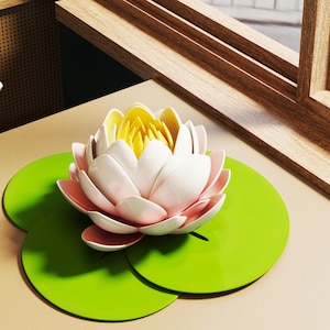 May include: A decorative lotus flower with white petals, pink accents, and a yellow center, resting on three bright green lily pads. The flower is set on a beige surface near a wooden window frame.