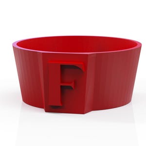 Può includere: Oggetto cilindrico rosso con una lettera "F" in rilievo. Ha una parte superiore ampia e aperta e un design sfaccettato. Probabilmente è un oggetto decorativo o un contenitore. Design semplice e moderno.