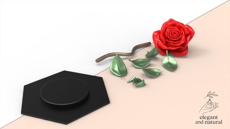 May include: A glossy red rose head, a curved brown stem, and several detached metallic green leaves arranged near a black hexagonal base. The image includes a small logo in the bottom right corner with the text elegant and natural.