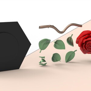 May include: A black hexagonal base with a circular center, a brown curved stem, several small green leaves, and a vibrant red rose blossom. The image includes a logo with a hand holding a leaf and the text elegant and natural.