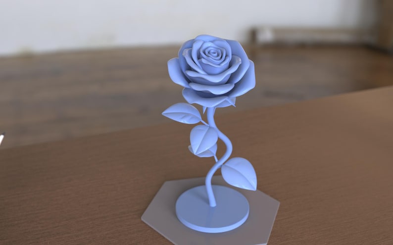 May include: A light blue rose sculpture featuring a detailed flower head with layered petals, a curved stem, and three leaves. The rose is attached to a circular base, which is mounted on a flat, light gray hexagonal platform for stability.