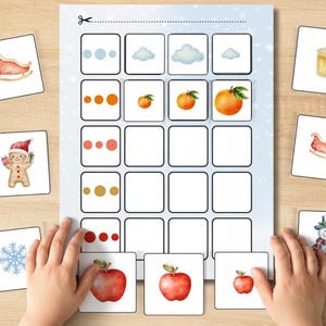 Puede incluir: Un juego de emparejamiento para niños con tarjetas ilustradas con temas de invierno y frutas. El juego incluye imágenes de un trineo, un hombre de jengibre, un copo de nieve, una vela y manzanas. El juego está sobre una superficie de madera.