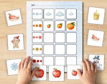 May include: A children's matching game with illustrated cards featuring winter and fruit themes. The game includes images of a sleigh, gingerbread man, snowflake, candle, and apples. The game is on a wooden surface.