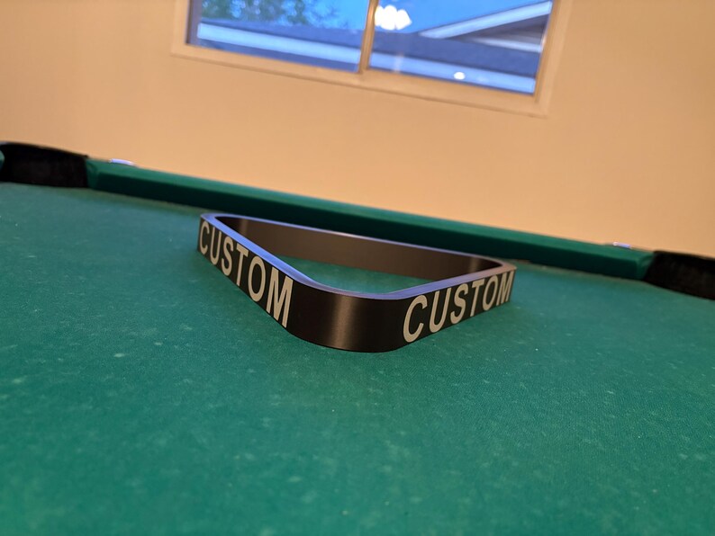 May include: A black pool table rack with the word "CUSTOM" printed on both sides in white lettering.