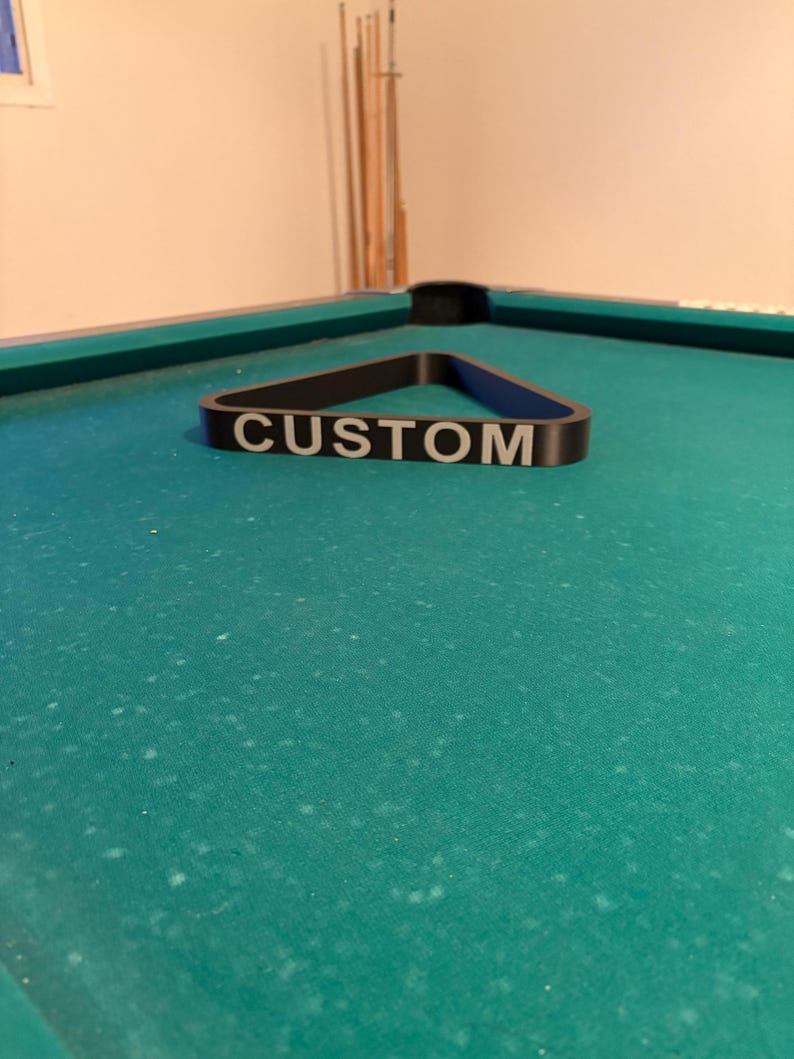 May include: A black pool triangle rack with the word "CUSTOM" printed in white on the front.