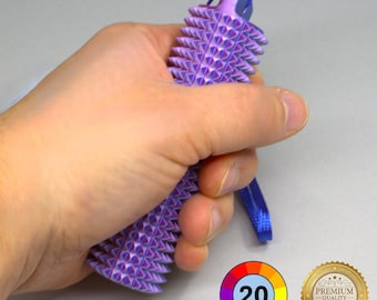 Puede incluir: Una herramienta de masaje púrpura con púas y un cordón azul se sostiene en una mano. La herramienta tiene una serie de púas triangulares. Una rueda de color con el número 20 y un sello dorado "Premium Quality" están en la esquina inferior derecha.