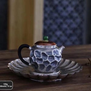 Puede incluir: Una tetera plateada con asa negra y tapa marr&oacute;n, sobre un platillo a juego. La tetera tiene un patr&oacute;n texturizado en forma de panal. La tapa est&aacute; rematada con una gema verde. Contiene 200ml y pesa 155g.