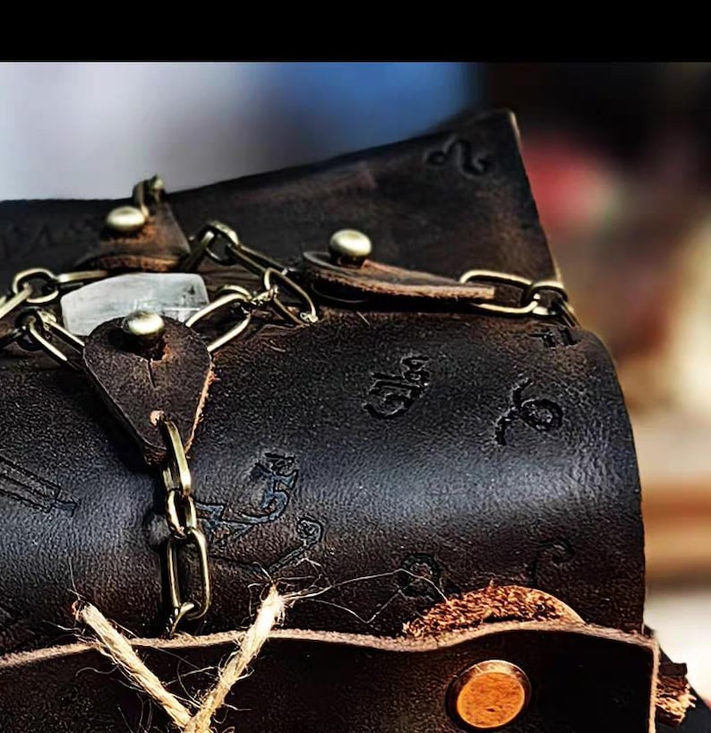May include: Close-up of a dark brown leather bag with a chain and clasp closure. The bag has embossed designs and metal rivets. A natural twine is attached to the bag.