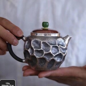Puede incluir: Tetera plateada con un patr&oacute;n texturizado en forma de panal. Tiene un asa oscura, una tapa marr&oacute;n y una piedra verde en la parte superior. La tetera tiene una capacidad de 200 ml y pesa 155 g.