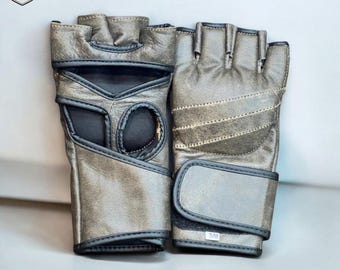 May include: A pair of gray fingerless weightlifting gloves. The gloves are made of leather with black trim and feature a wrist strap with a hook and loop closure. The gloves have a padded palm and finger holes for grip and comfort. The gloves are designed for weightlifting and other fitness activities.