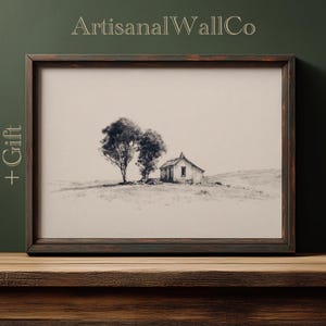 May include: Framed black and white print of a rural landscape featuring a small house and two trees. The artwork is in a dark wooden frame and has the text "ArtisanalWallCo" at the top. The word "Gift" is on the left side of the frame.