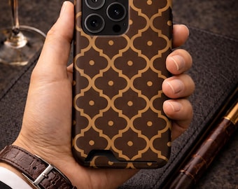May include: A brown and gold patterned phone case. The case features a repeating quatrefoil design. The phone case is held in a hand, with a brown leather watch and a pen visible in the background. The case is designed to fit a modern smartphone.