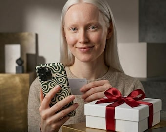 May include: A smartphone case featuring a dark green and cream-colored wavy abstract pattern, paired with a white gift box tied with a red satin ribbon. The case includes a card slot, and the text on the image reads PREMIUM GIFT-READY SET.