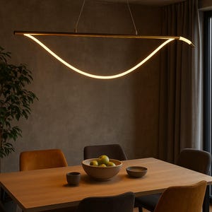以下が含まれることがあります： 木製のテーブルと椅子を備えたモダンでミニマリストなダイニングルーム。テーブルの上には、長く湾曲したゴールドトーンのLED照明器具が吊り下げられています。緑色の果物が入った木製のボウルと小さなセラミックボウルがテーブルにあります。