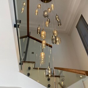 May include: A modern chandelier with multiple glass pendant lights of varying shapes and sizes. The lights are suspended from a circular brass ceiling fixture. The staircase has glass panels and wooden handrails.