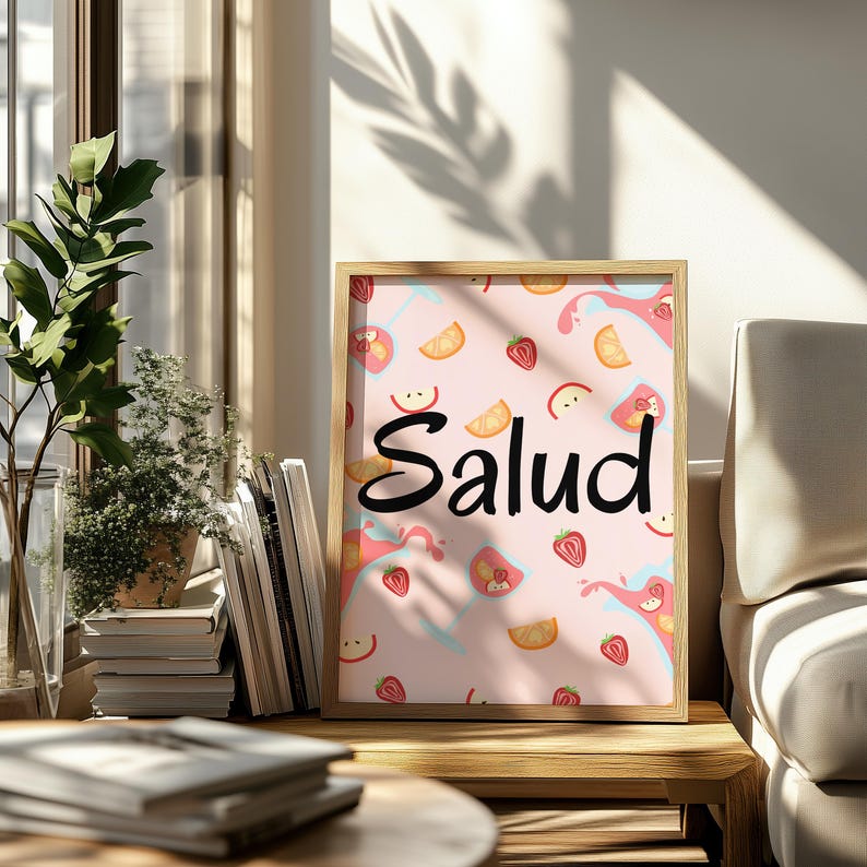 Puede incluir: Un cuadro enmarcado con la palabra "Salud" en escritura negra. El fondo es rosa con ilustraciones de rodajas de fruta y salpicaduras. El marco es de color madera clara, y el cuadro se exhibe sobre una mesa de madera.
