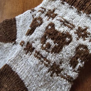 Pode incluir: Meias de tricô marrom e branco com um desenho de urso marrom. As meias têm uma bainha marrom.