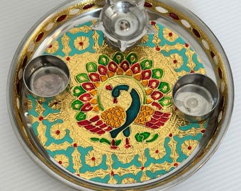 May include: A decorative silver-colored plate with a gold, teal, and red peacock design in the center. The plate has a raised edge with red accents and includes three small metal bowls. The peacock is depicted with vibrant colors.