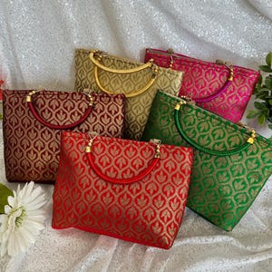 May include: A collection of six small, rectangular handbags in various colors, including red, gold, green, and pink. Each bag features a gold leaf pattern and a matching handle. The bags are arranged on a white, sequined surface.