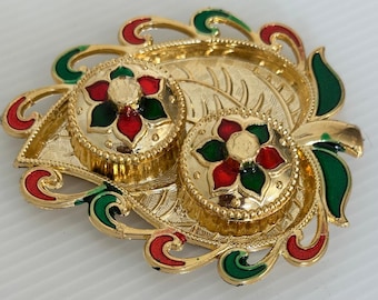 May include: An ornate gold-coloured decorative tray with two lidded containers. The tray and containers feature red and green floral and leaf designs. The tray has a detailed, embossed pattern, suitable for display or serving.