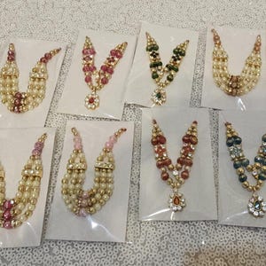May include: A collection of beaded necklaces in various colors, including cream, pink, red, green, and blue. Each necklace is displayed on a white card, with a gold-colored pendant.