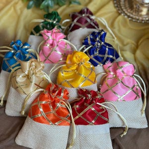 May include: A collection of small, colorful drawstring bags. The bags are made of burlap with satin tops in various colors, including pink, blue, yellow, and orange, with gold crisscross patterns. Each bag has a matching drawstring.