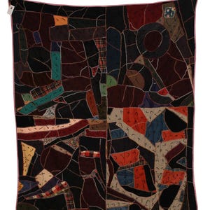 May include: A rectangular quilt featuring a patchwork design of various fabric scraps in black, red, blue, orange, and green. The pieces are joined with white zigzag stitching, and the entire quilt is finished with a light pink fabric border.