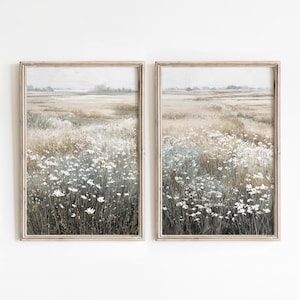 May include: Two framed landscape prints. Each print depicts a field of wildflowers in shades of white, green, and brown. The artwork has a vintage aesthetic, with a soft, muted color palette. The frames are a light, natural wood color.