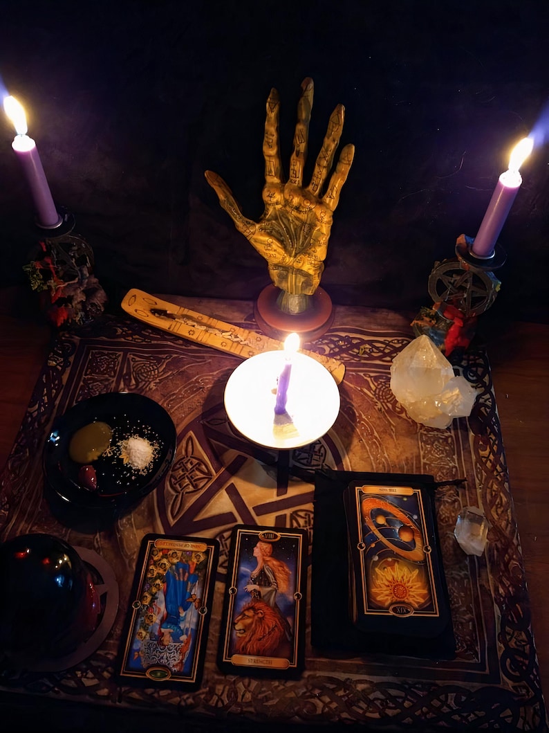 Puede incluir: Una escena m&iacute;stica con una estatua de mano dorada, velas encendidas, cartas del tarot y un cristal. La disposici&oacute;n incluye un cuenco con sal y otros elementos, creando una atm&oacute;sfera de adivinaci&oacute;n y pr&aacute;ctica espiritual.